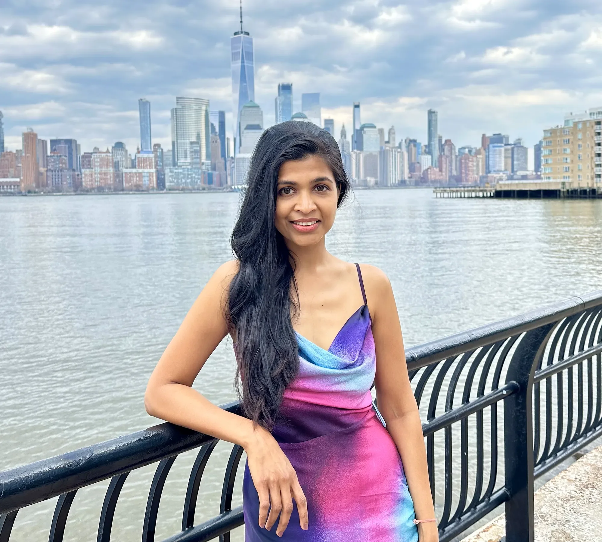Artist Prachi Gawas standing beside a waterfront with the New York City skyline in the background
