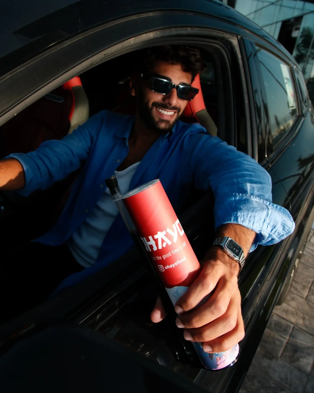 Man leaning out of a car window holding an Ohayo