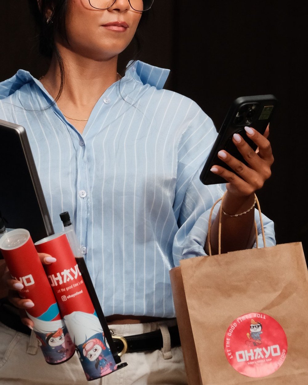 Woman on her phone with Ohayo tubes and a takeaway bag