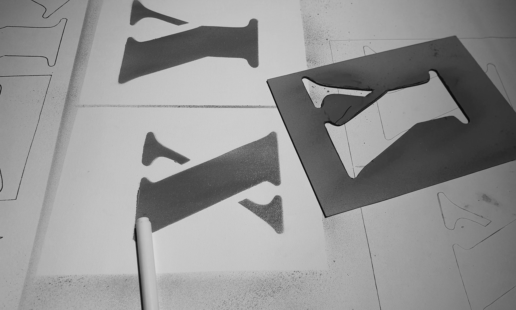 Black and white photo showing fabric cutouts of the letter 'F' on paper patterns, with a white marker and a cardboard box with an 'F' cutout inside, on a white surface.