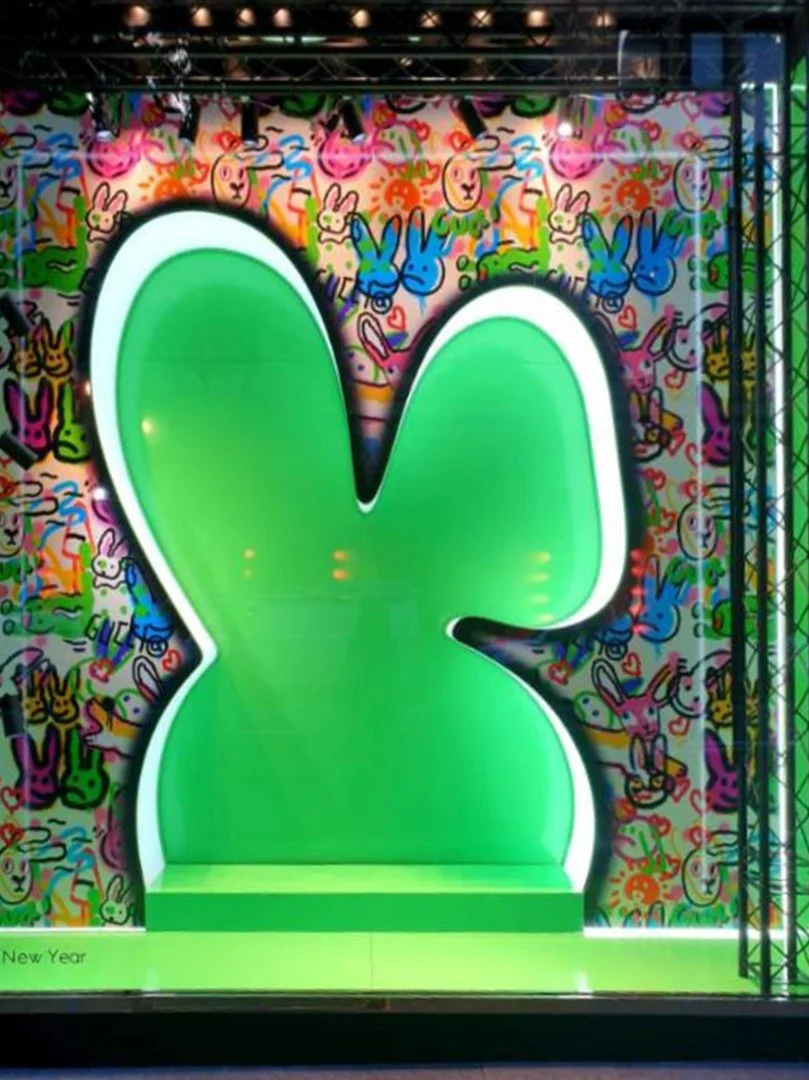 Custom high end luxury retail brands window dressing, installation.A large, illuminated green bunny silhouette with a white outline against a colorful, patterned background featuring numerous smaller bunny images in various colours. HR Productions Sy