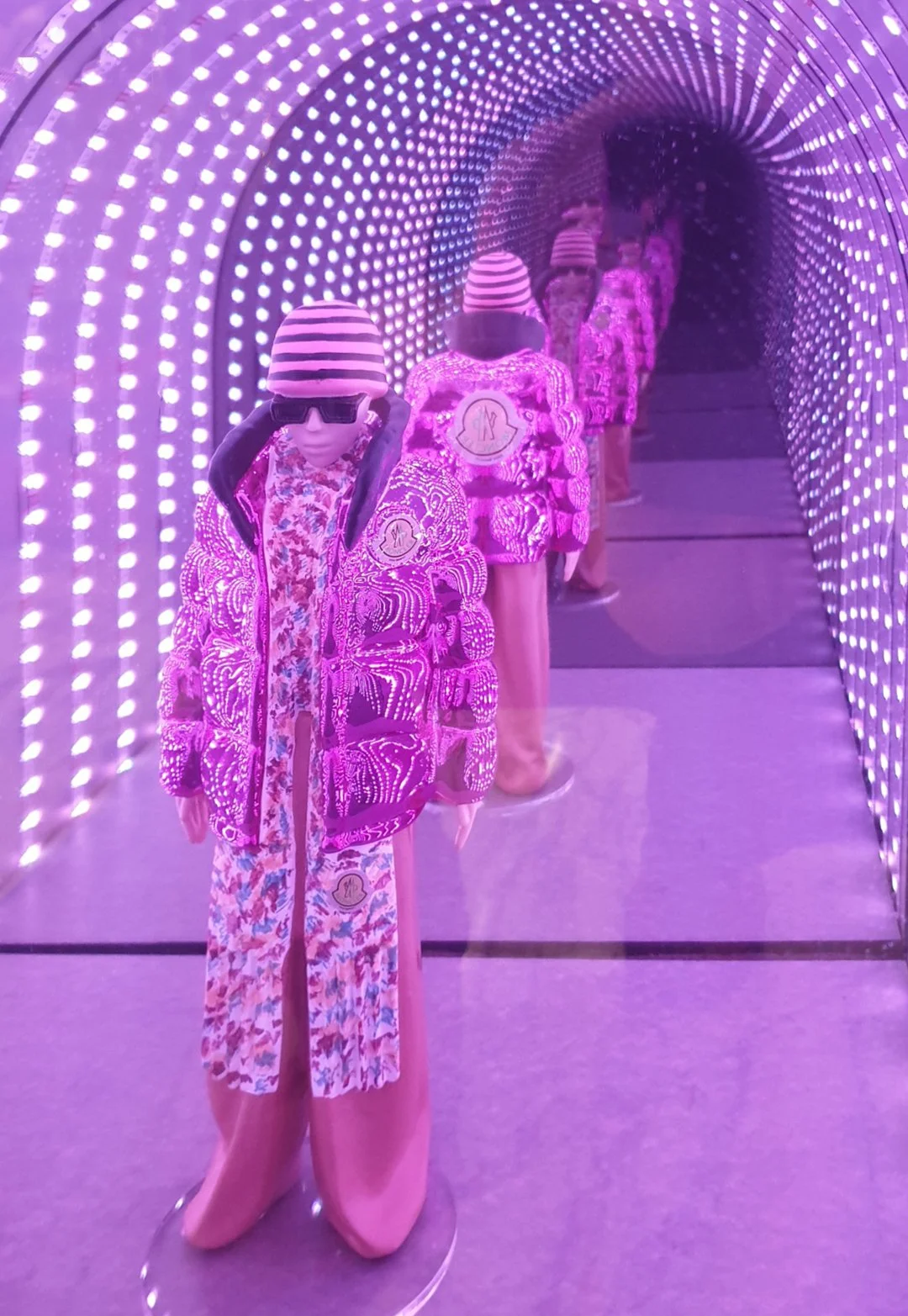 Custom high end luxury retail brands window dressing, props, installation.Mannequins dressed in colorful, patterned clothing with striped hats, positioned in a line inside a tunnel made of purple LED lights. HR Productions Sydney
