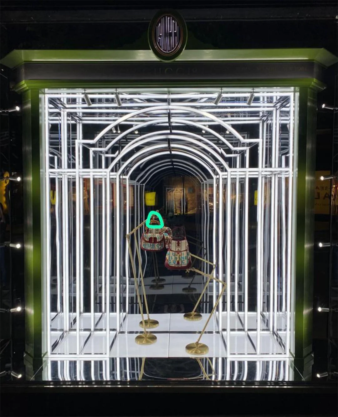 Neon-lit display featuring two backpacks on gold stands, with a geometric metal frame structure and illuminated archways, creating a tunnel-like visual effect. Custom high end luxury retail brands window dressing, installation HR Productions Sydney