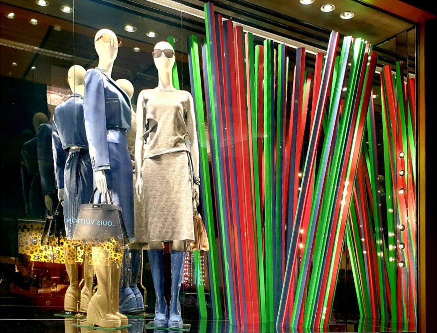 Custom high end luxury retail brands window dressing, installation.Store window display with mannequins dressed in stylish clothing, with colorful red, green, and blue striped decor in the background. HR Productions Sydney