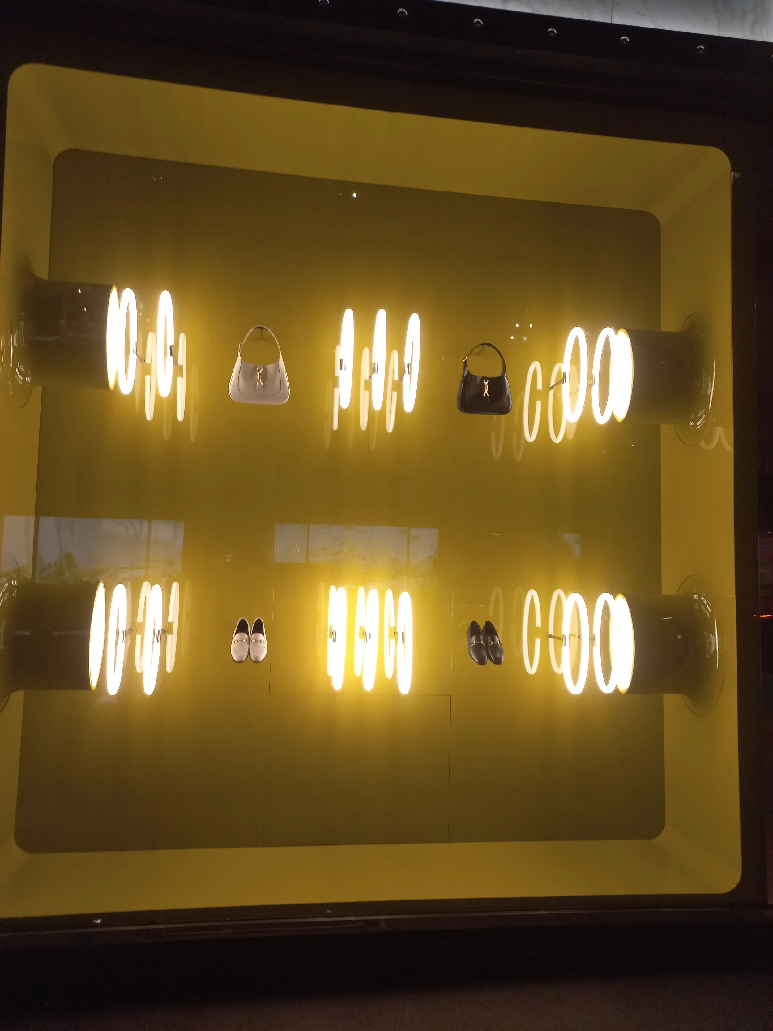 Display case with shoes and handbags illuminated by bright lights, set against a yellow background. Custom built props, Custom high end luxury retail HR Productions Sydney