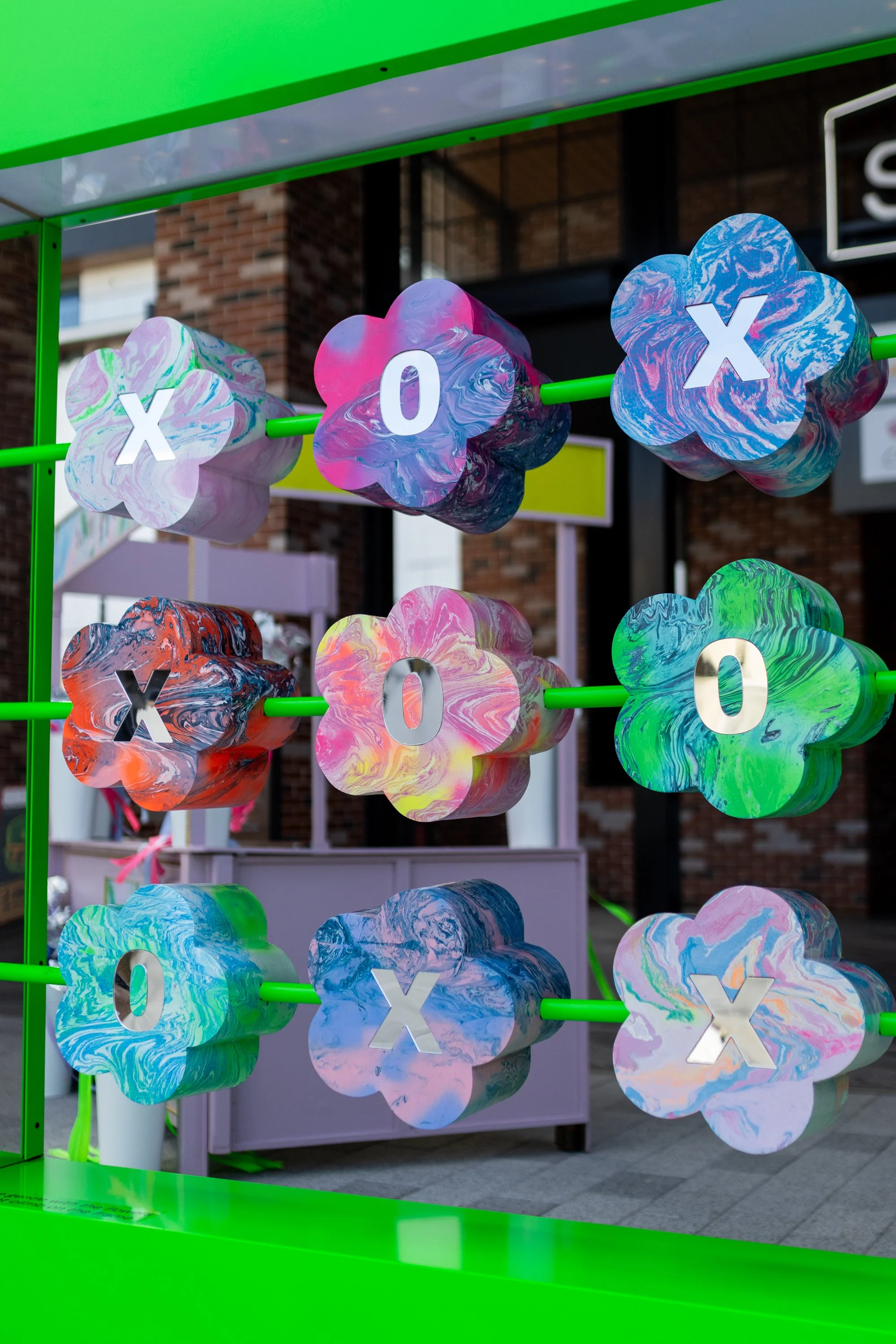 HR Productions Custom built artist collaboration. ACID FLWRS Perth outdoor installation. neon colours. Colourful dipped florals on green display stand in an outdoor setting, neon green large stand. Floral noughts and crosses