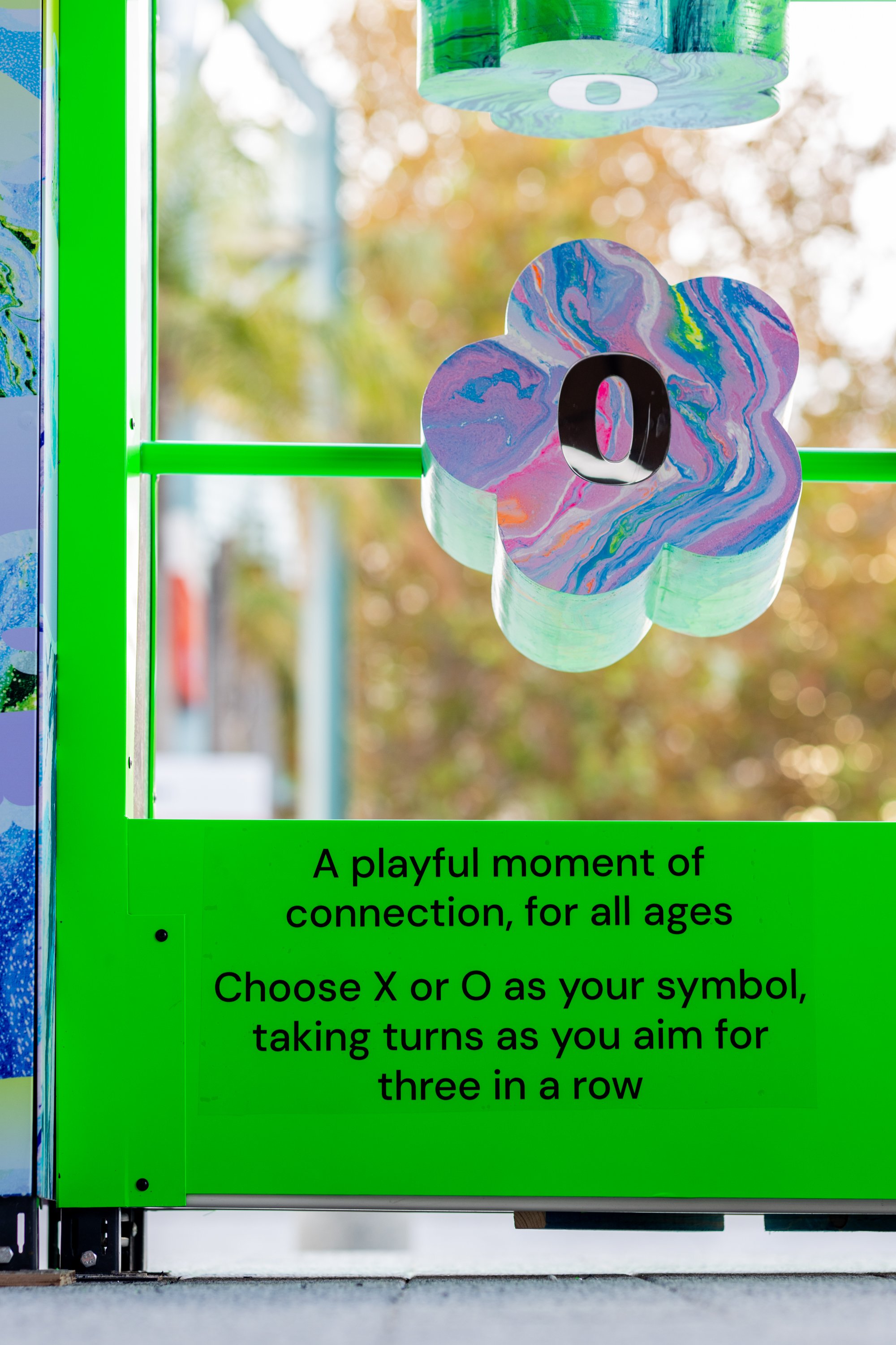 Close-up of a colorful, marbled flower-shaped sign with a large black number '0' in the center, attached to a bright green frame. ACID FLWRS, HR Productions installation Perth. 