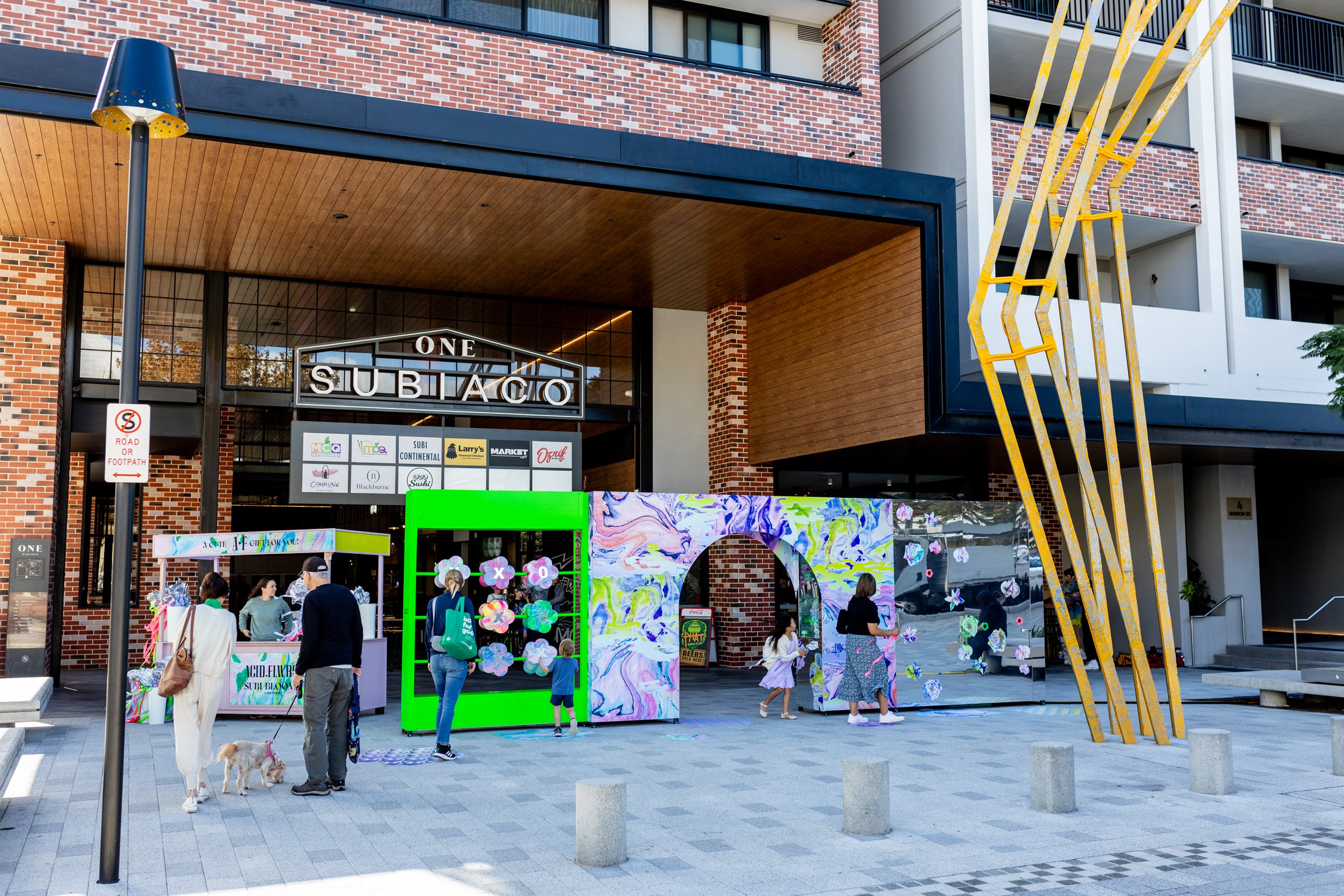 HR Productions Custom built artist collaboration. ACID FLWRS Perth outdoor installaton. neon colours. Colorful dipped florals on green display stand in an outdoor setting, neon green large stand