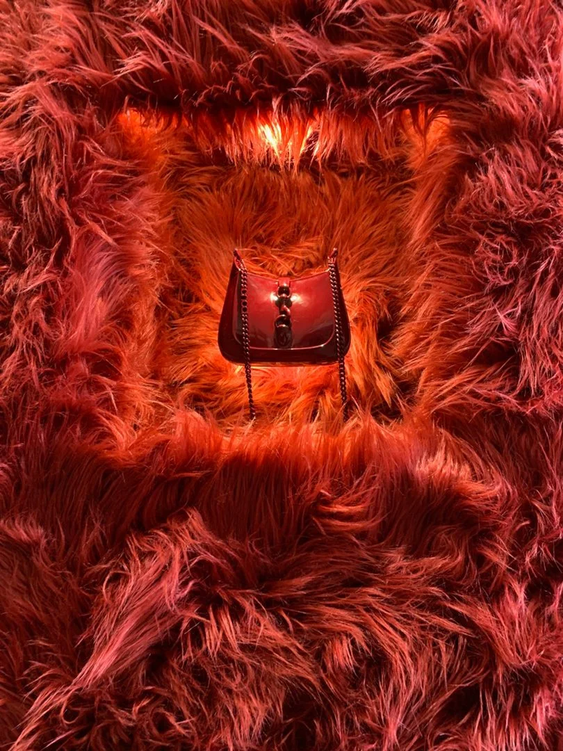A luxurious red fur coat with a small red handbag placed in the center, surrounded by the fluffy fur. Luxury Brands Sydney, Luxury window dressing, custom props and installation