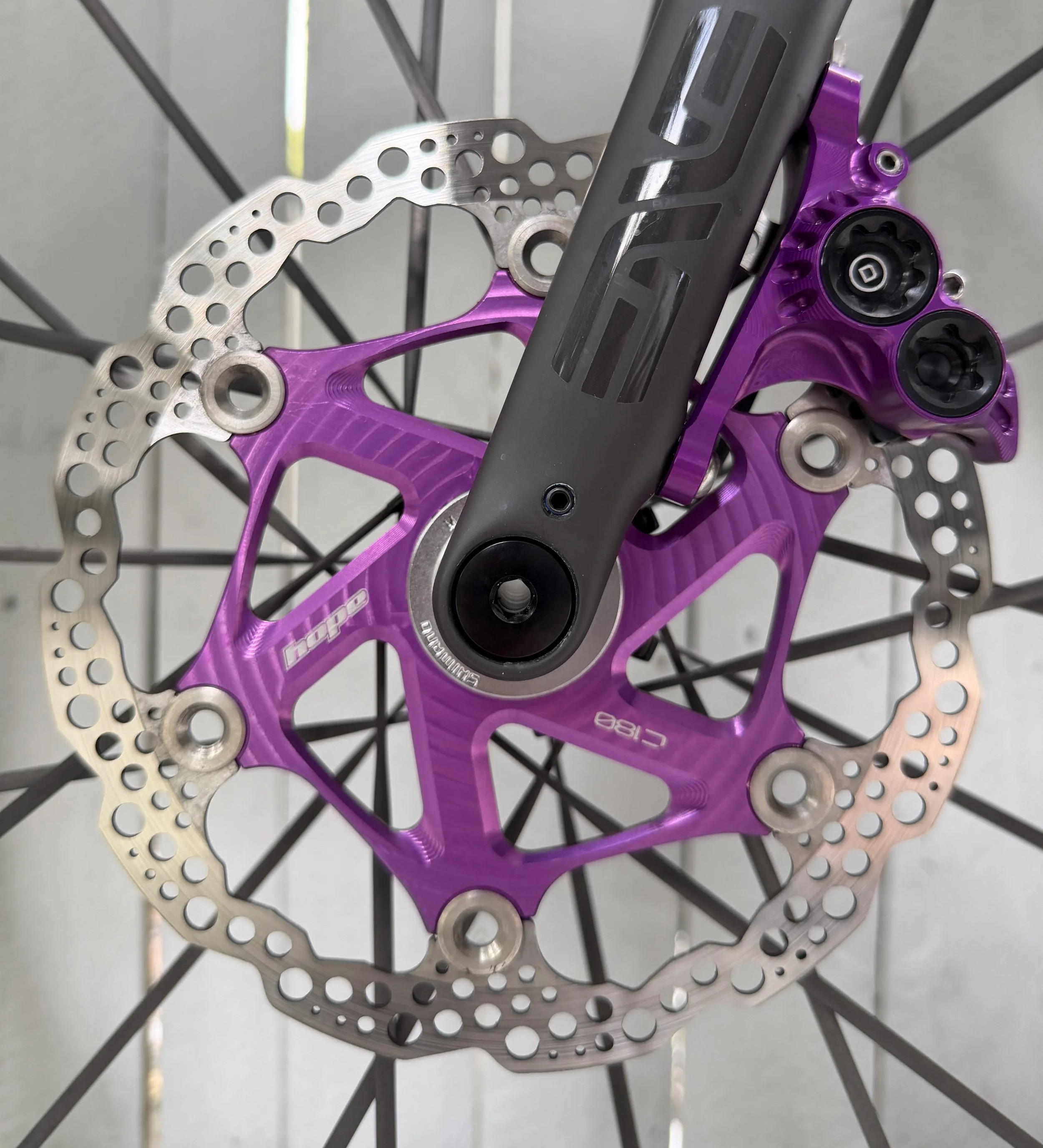 Close-up view of a mountain bike disc brake rotor with purple anodized mount, installed on a bicycle wheel with spokes visible in the background.
