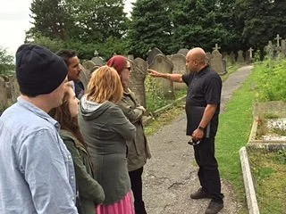 Group gathered in cemetery listening to guide speaking on a Beatles tour