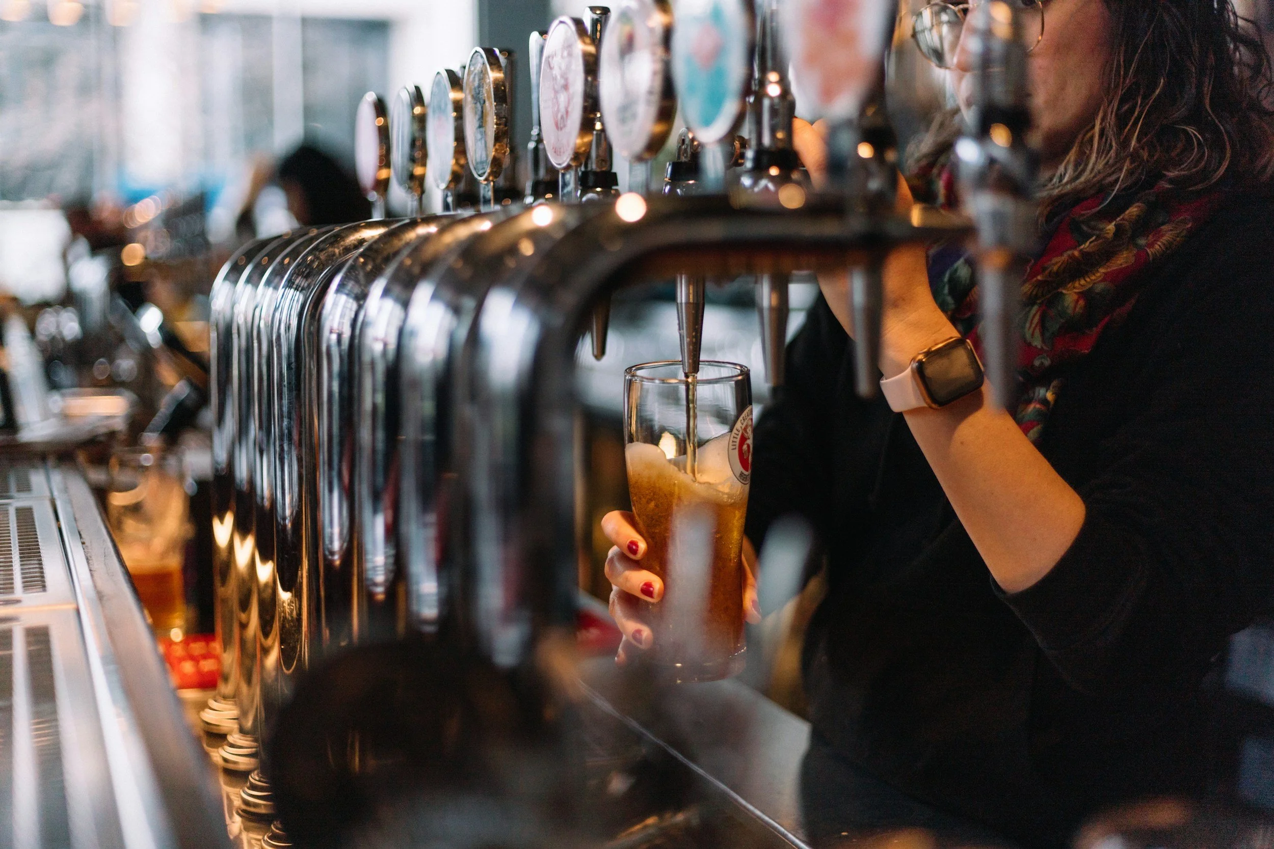 Woman pouring draft beer from tap at bar