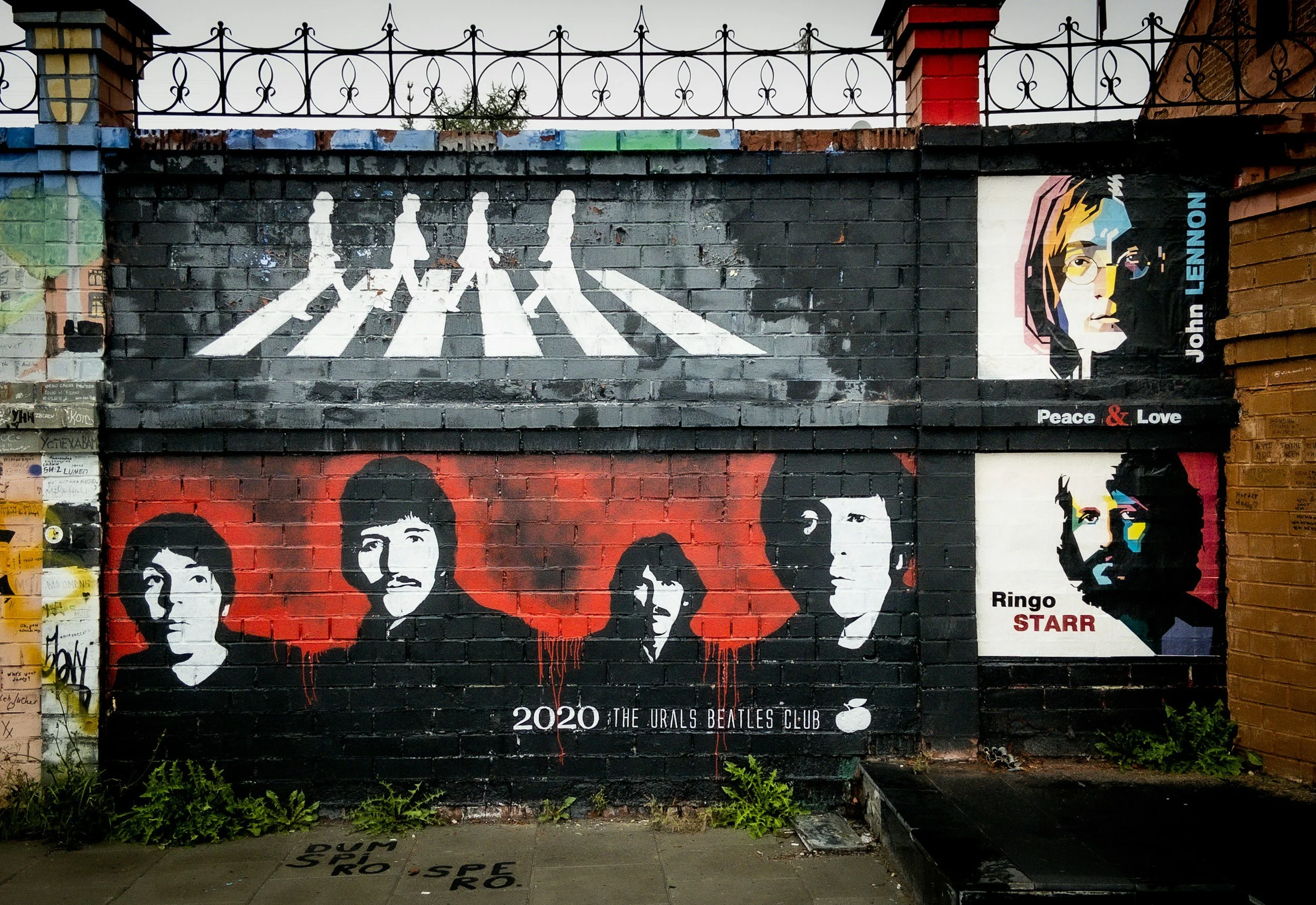 Beatles mural with crosswalk silhouettes and John Lennon portrait on brick wall