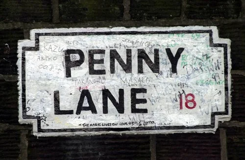 Street sign reading 'Penny Lane' with various graffiti and signatures in multiple colors.