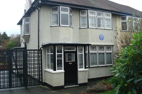 Aunt Mimi’s house ‘Mendips’ in Liverpool, a white two‑storey National Trust building with a curved bay window, black front gate and surrounding greenery