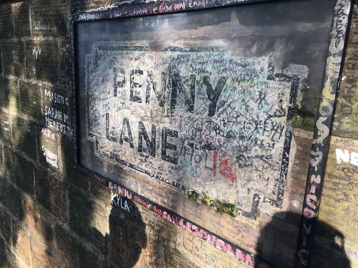 Penny Lane street sign in Liverpool on a weathered brick wall covered with graffiti and handwritten signatures