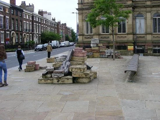 Suitcase sculpture installation outside the Liverpool art school, with stacked bricks, stones and a bent metal bench beside the building’s large windows