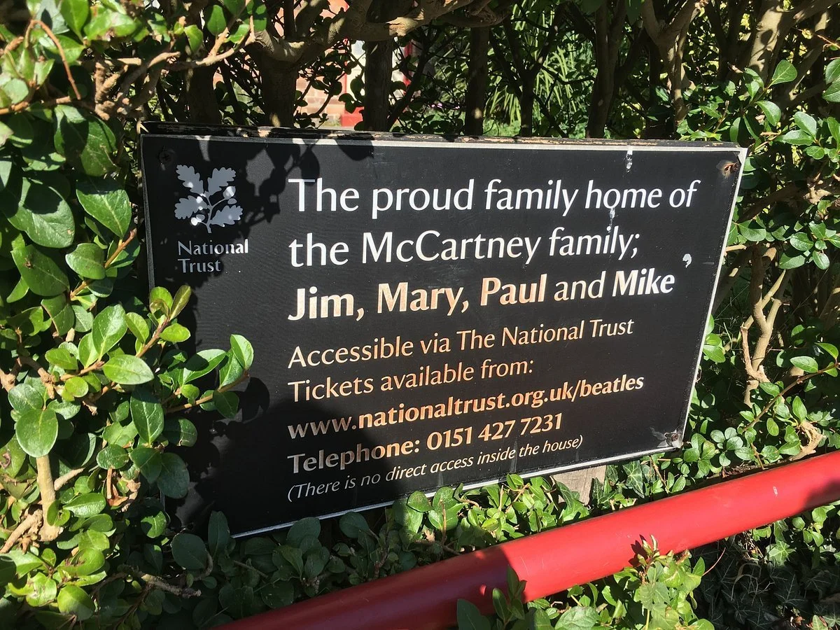 Black National Trust sign surrounded by greenery marking the McCartney family home in Liverpool, with information about access and tickets