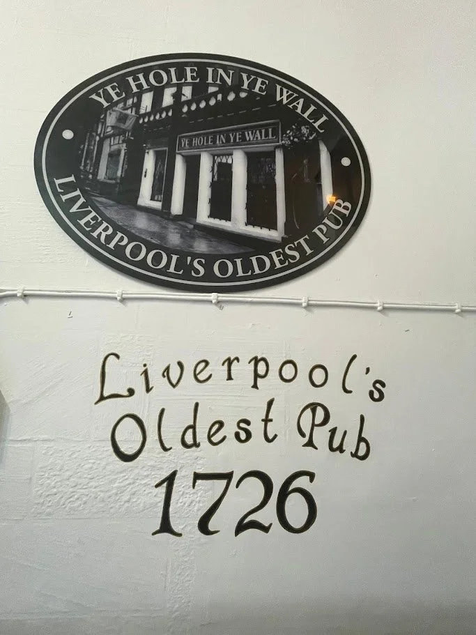 Sign and wall decoration for Liverpool's oldest pub, established in 1726, with a black oval sign featuring an image of the pub and text reading "Ye Hole in Ye Wall" and "Liverpool's Oldest Pub."