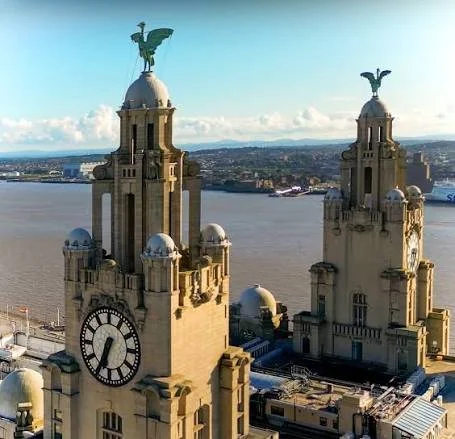Two historic clock towers with eagle sculptures on top, overlooking a river and cityscape under a partly cloudy sky.