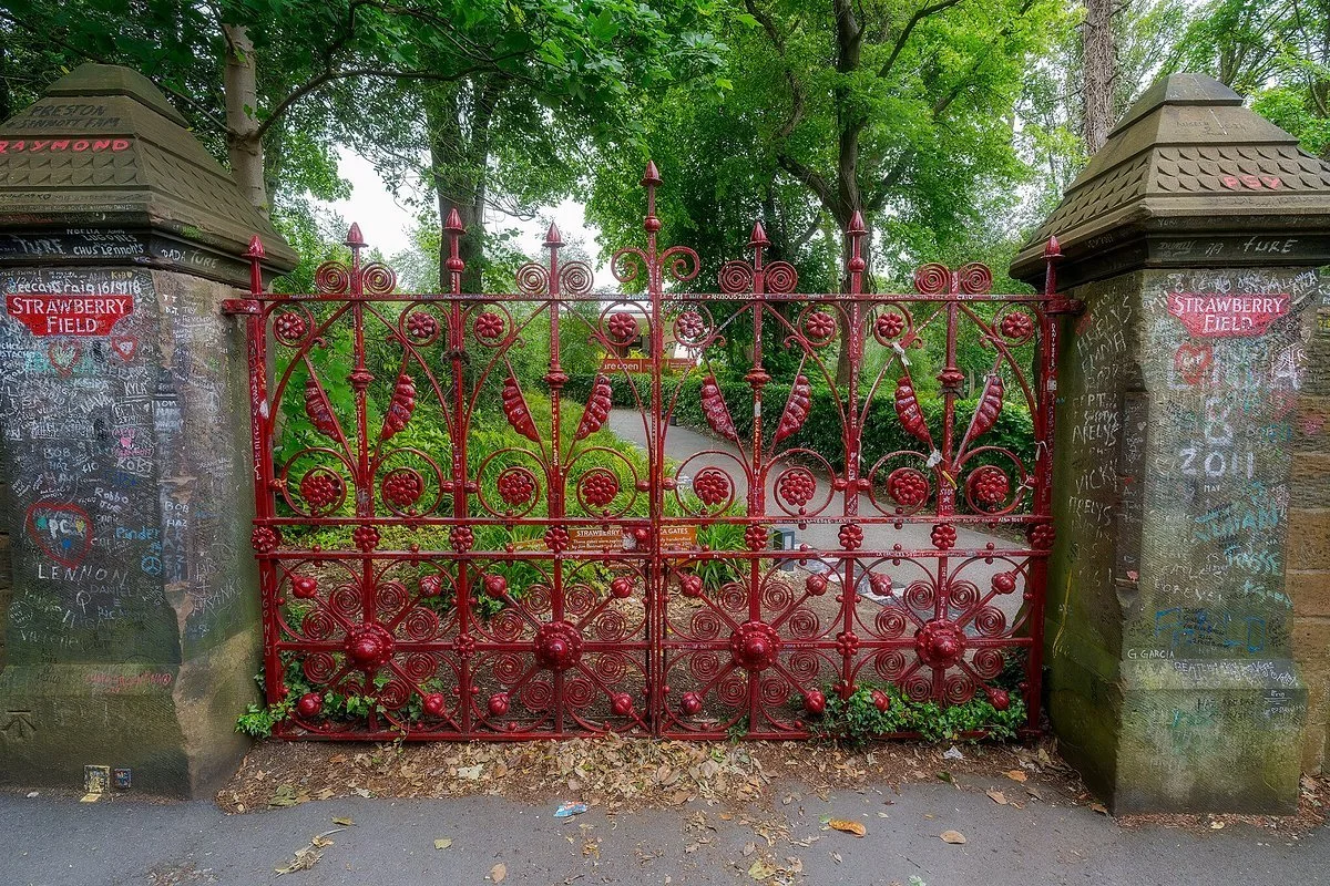 Red Strawberry Field gates in Liverpool with decorative ironwork, flanked by brick pillars covered in chalk graffiti