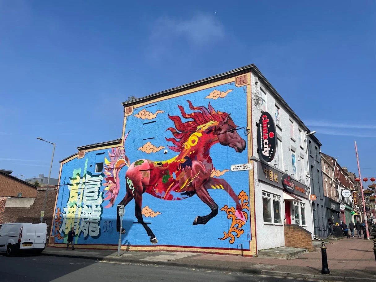 Colourful mural of a fiery red horse with flowing mane and tail on a Liverpool Chinatown building, with clouds and Chinese characters behind