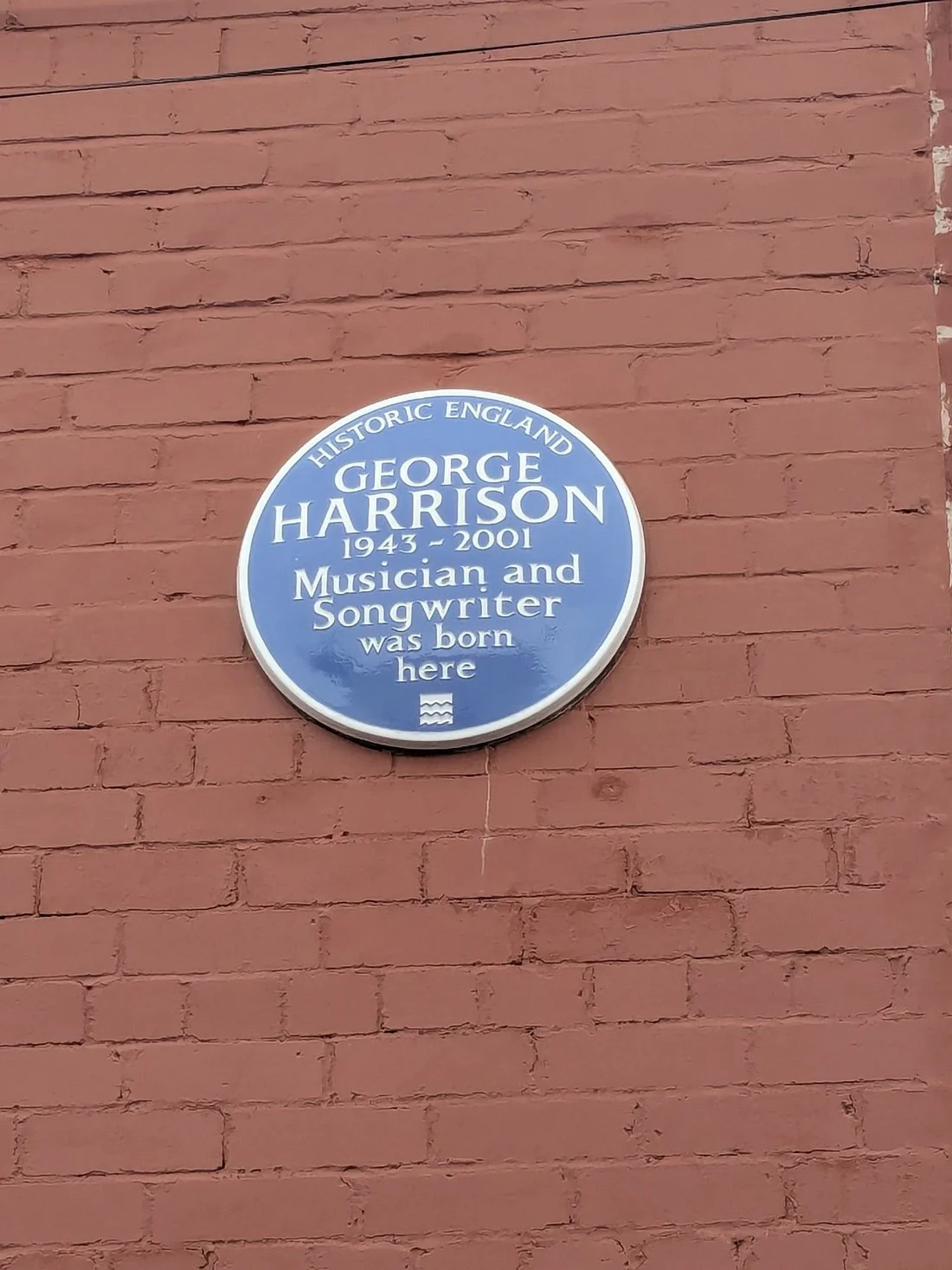 Blue plaque marking George Harrison’s birthplace on a red brick wall in Liverpool, commemorating him as a musician and songwriter