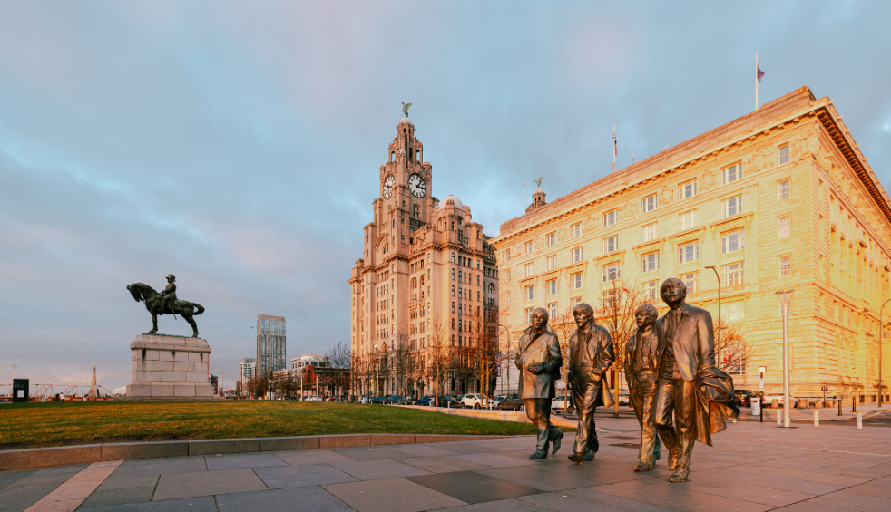 Bronze statues of The Beatles walking in front of the Royal Liver Building in Liverpool at sunset