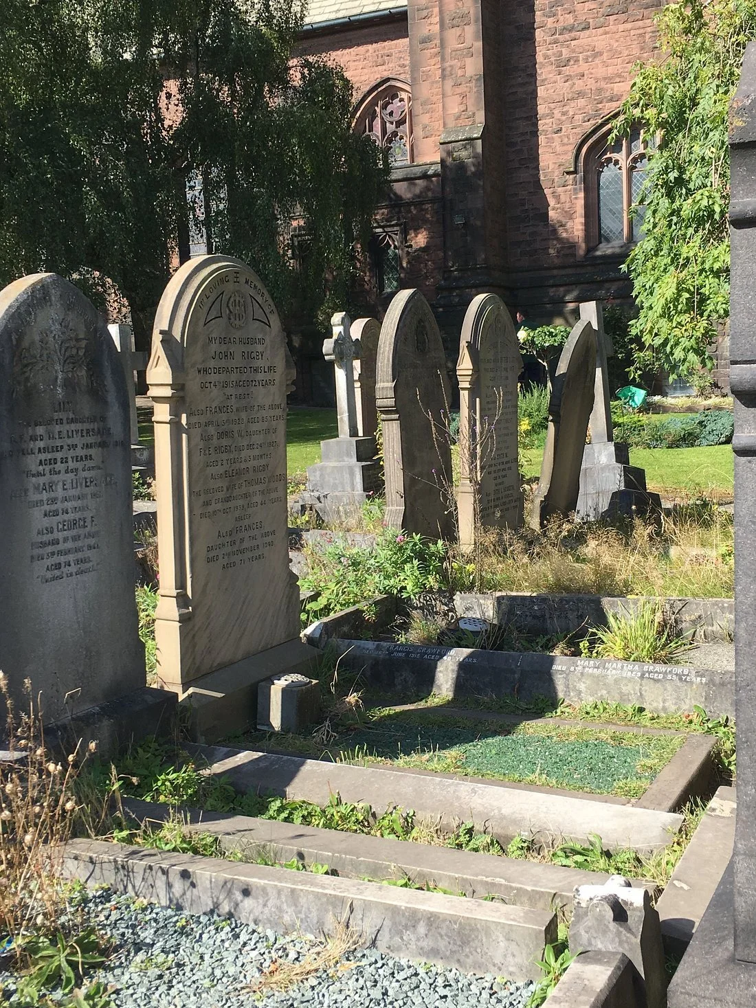 d Liverpool cemetery with weathered gravestones surrounded by grass and plants, with a brick church building in the background