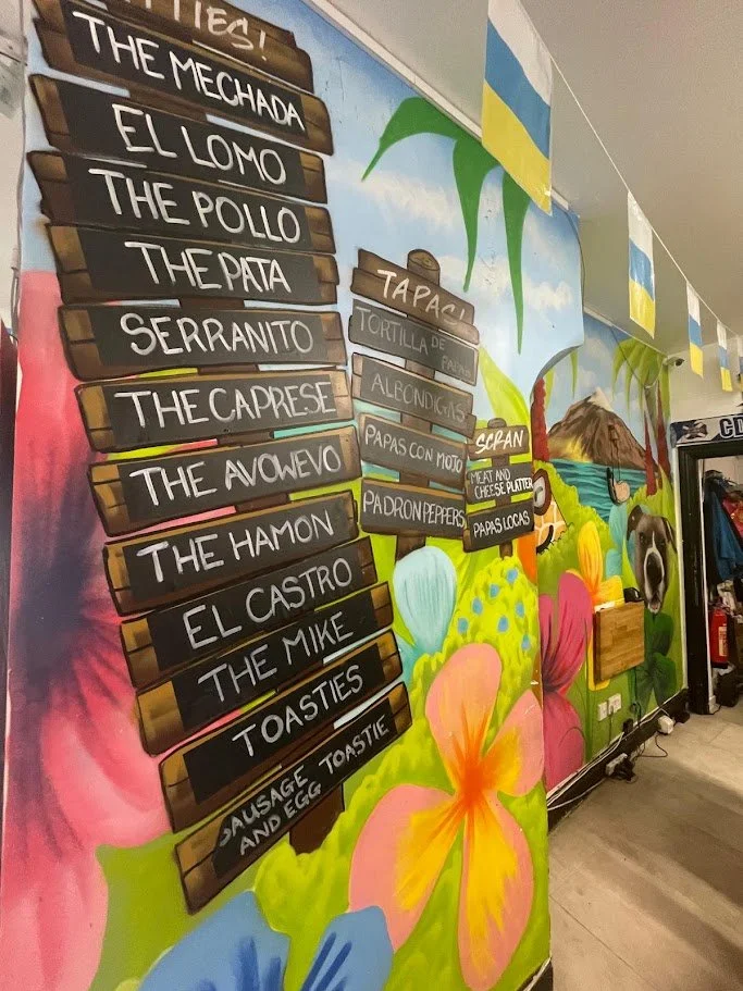 Colourful menu inside a Liverpool restaurant with menu items on blackboards set against a tropical background with flowers