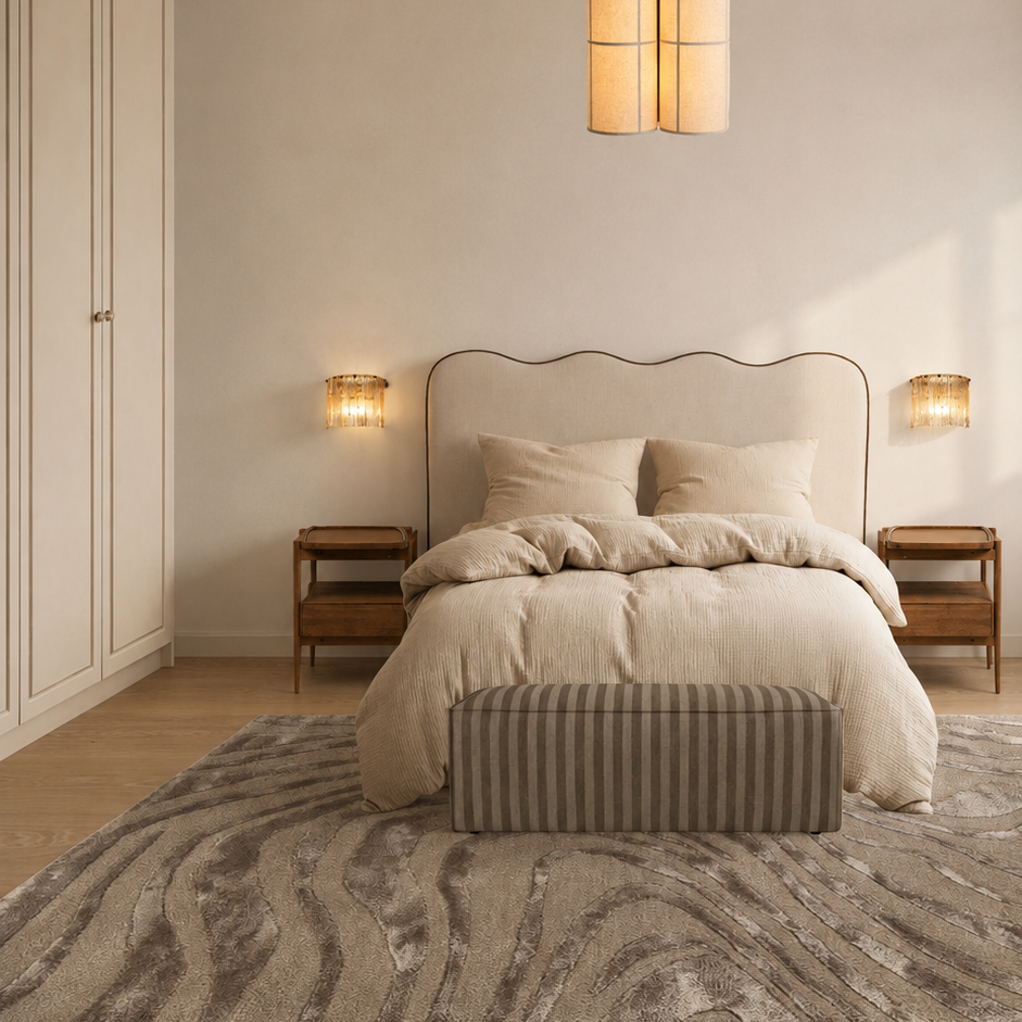 A cozy bedroom with a beige bed, two bedside tables with lamps, a striped bench at the foot of the bed, and a textured rug on a wooden floor.
