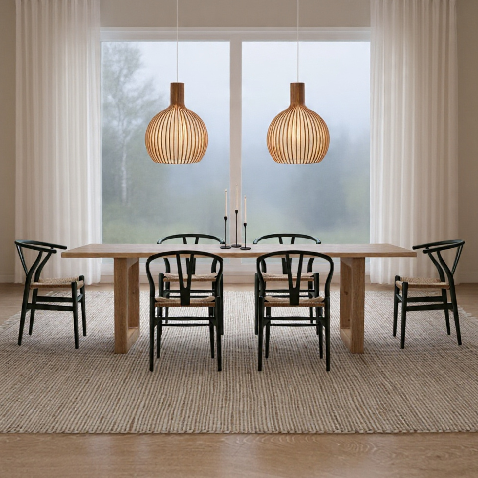 Modern dining room with a wooden table, six black chairs, two large wooden pendant lights, a large window with white curtains, and a neutral rug over hardwood flooring.