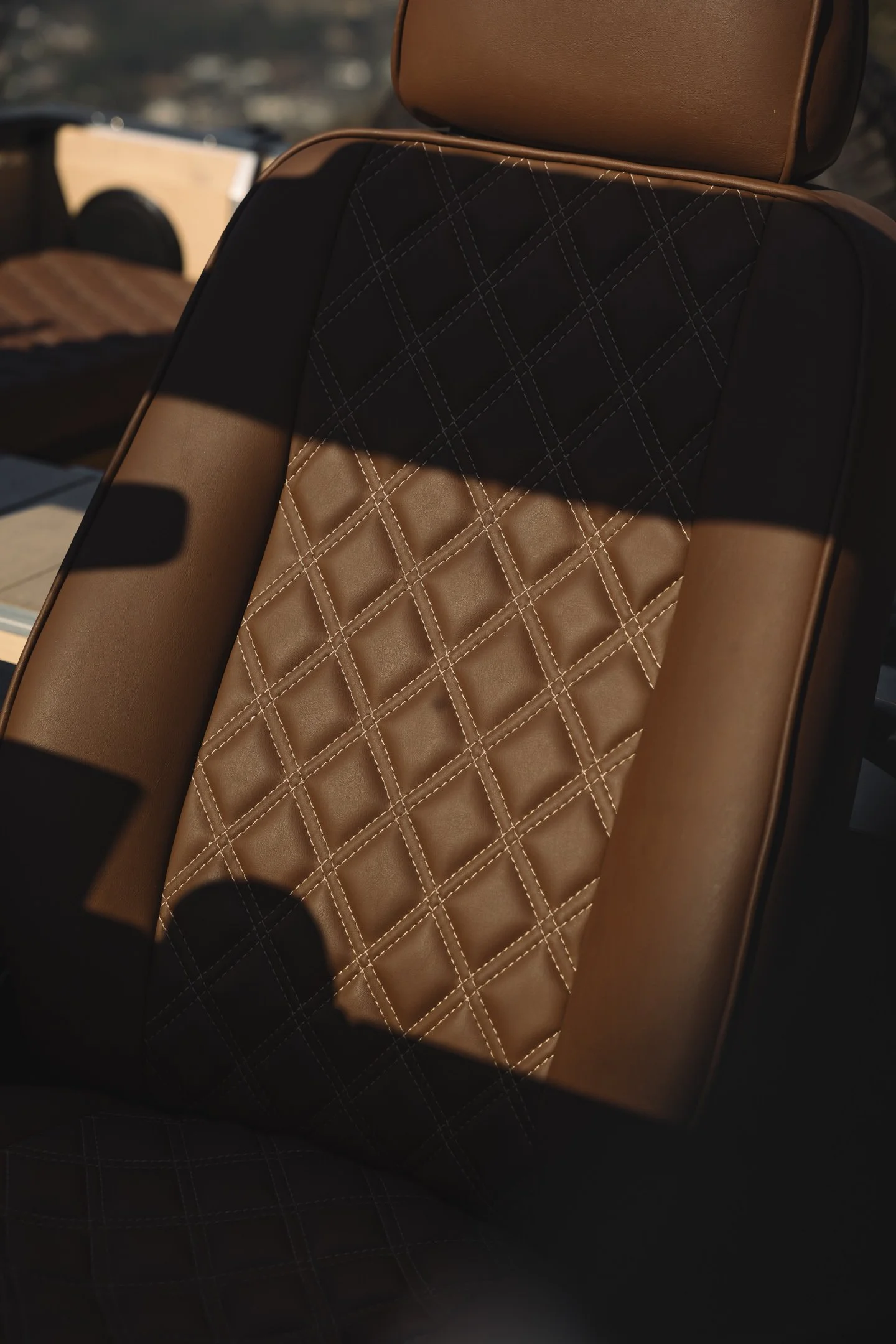Close-up of a car seat with tan and black quilted leather upholstery illuminated by sunlight.