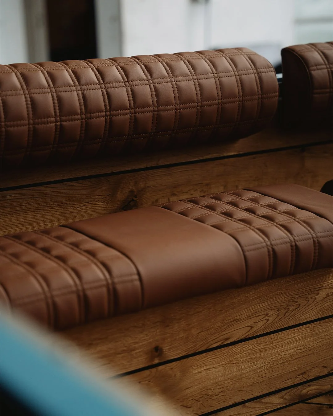 Close-up of brown quilted leather bench seating with wooden base.