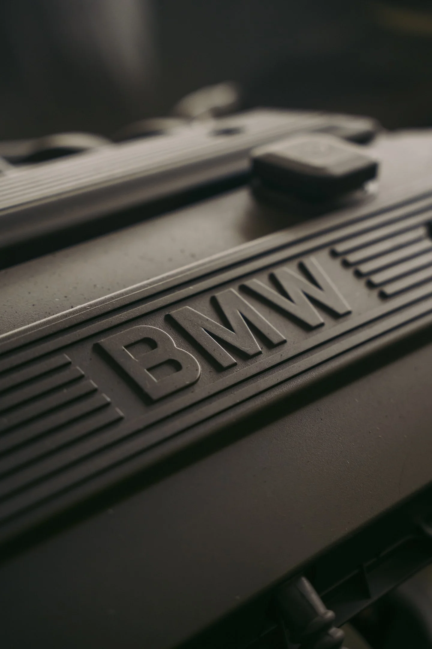 Close-up of a black device with the word 'BMW' engraved on it, with a textured surface and a power cable attached.