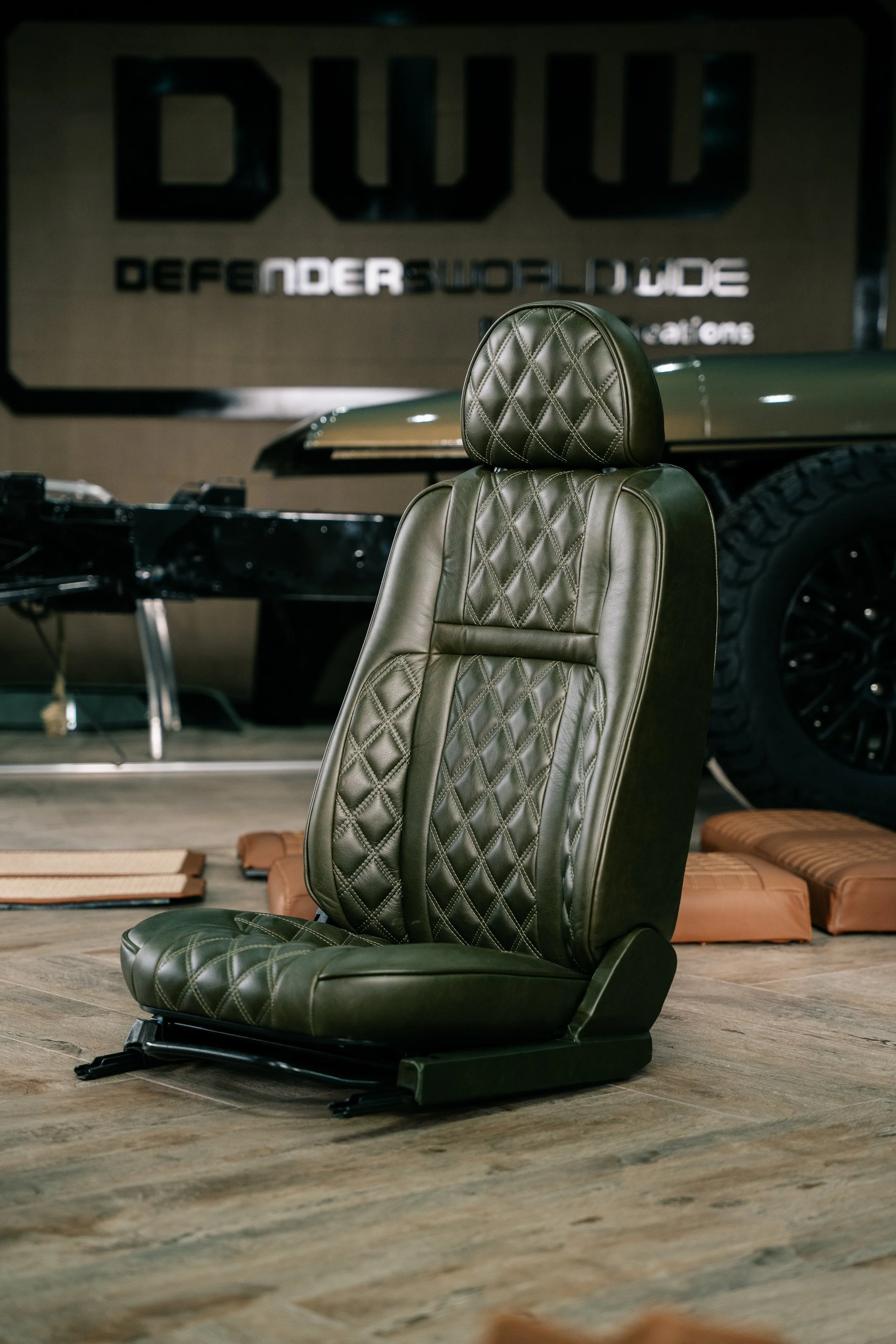 A black leather car seat with diamond stitching, placed on a wooden floor in a showroom or garage setting. 