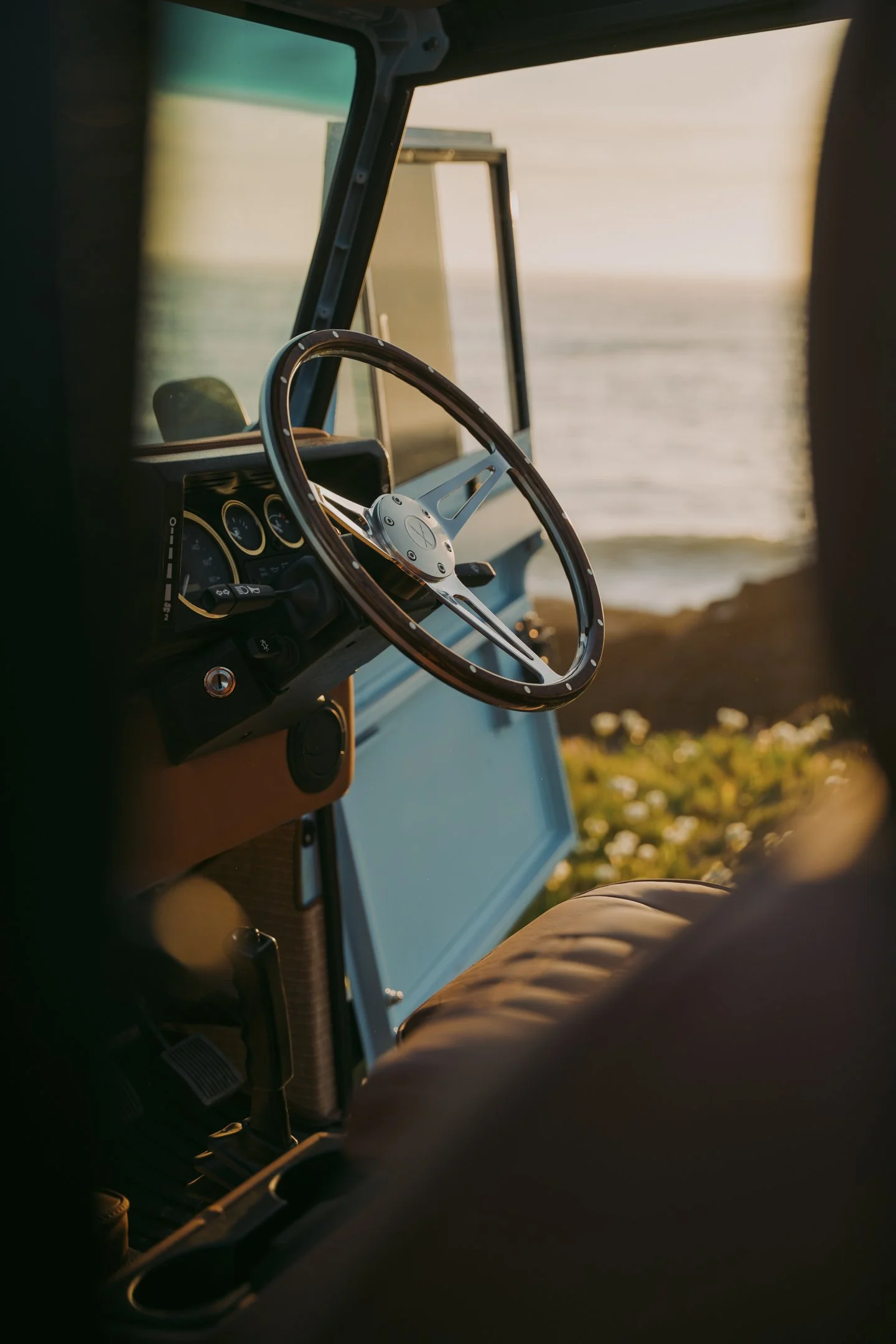 View from inside a vehicle, showing the dashboard and steering wheel, with a body of water and sunset in the background.