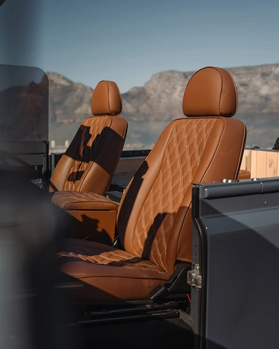Two brown leather seats inside a vehicle, with a scenic mountain view in the background.