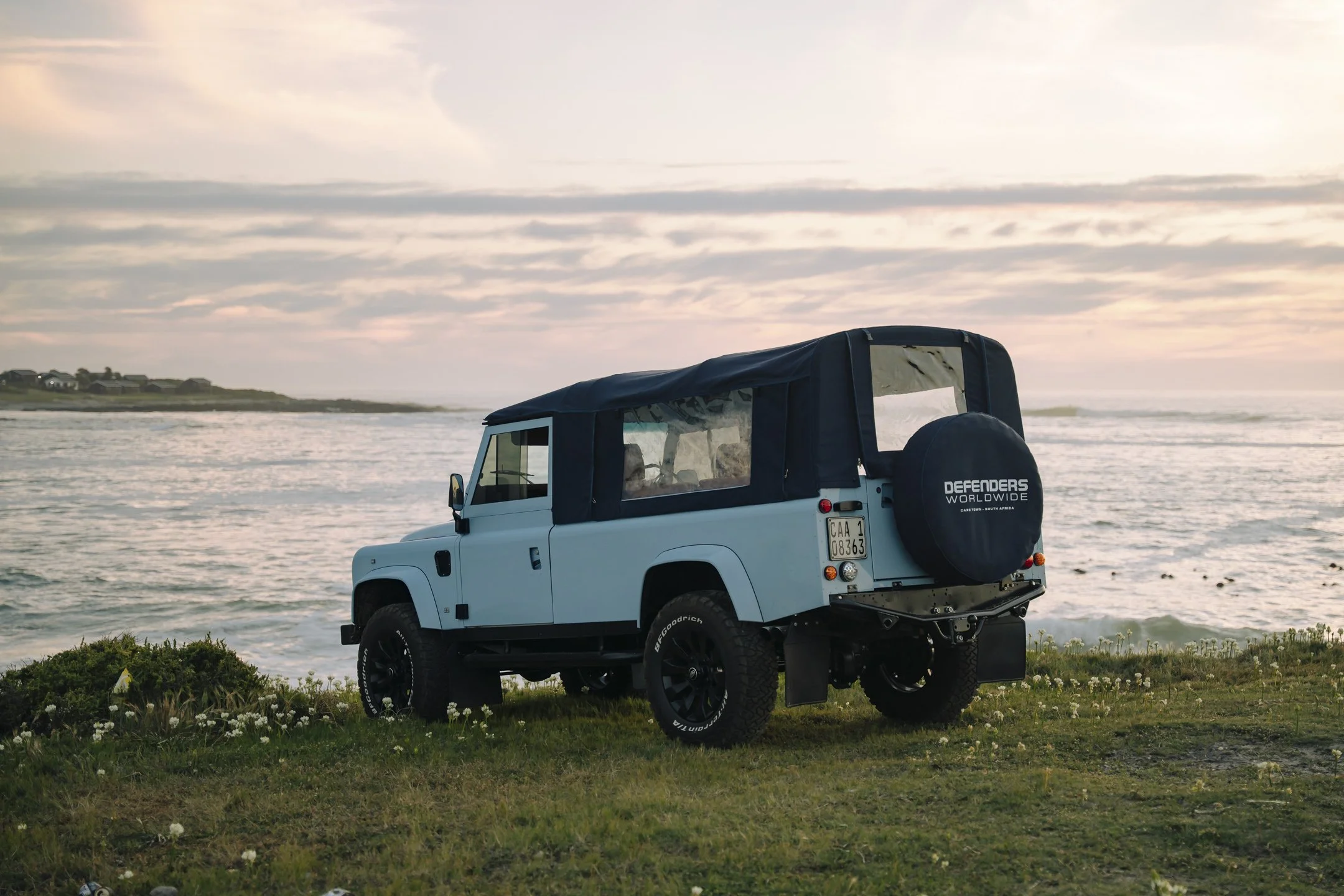 A white off-road vehicle parked on grassy terrain near the shoreline with the ocean and cloudy sky in the background.