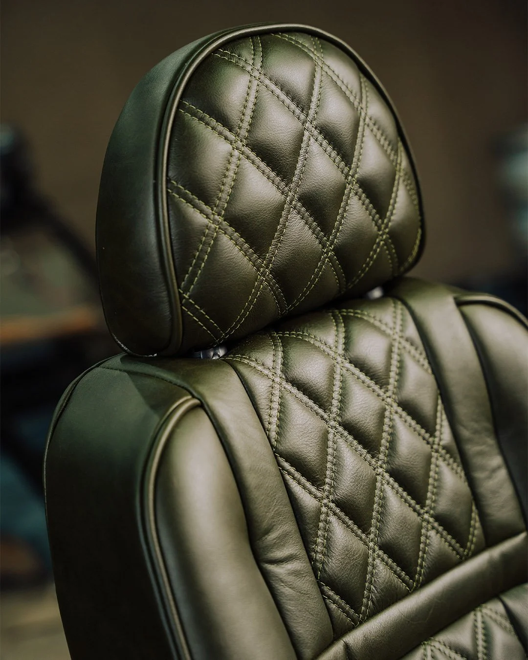 Close-up of a black leather car seat with a diamond quilt pattern and green stitching.