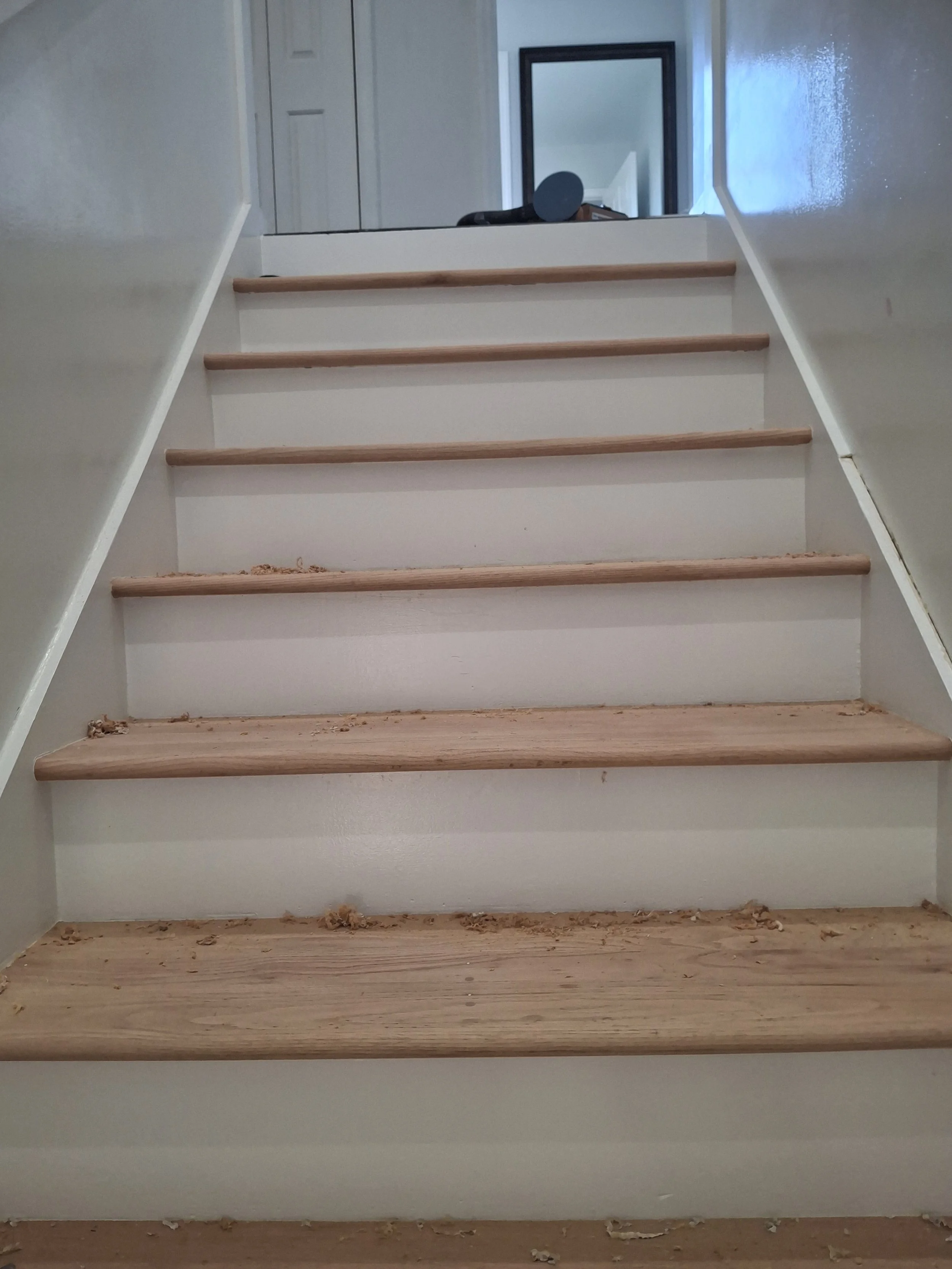 Empty wooden staircase with debris at the bottom and a mirror in the background.