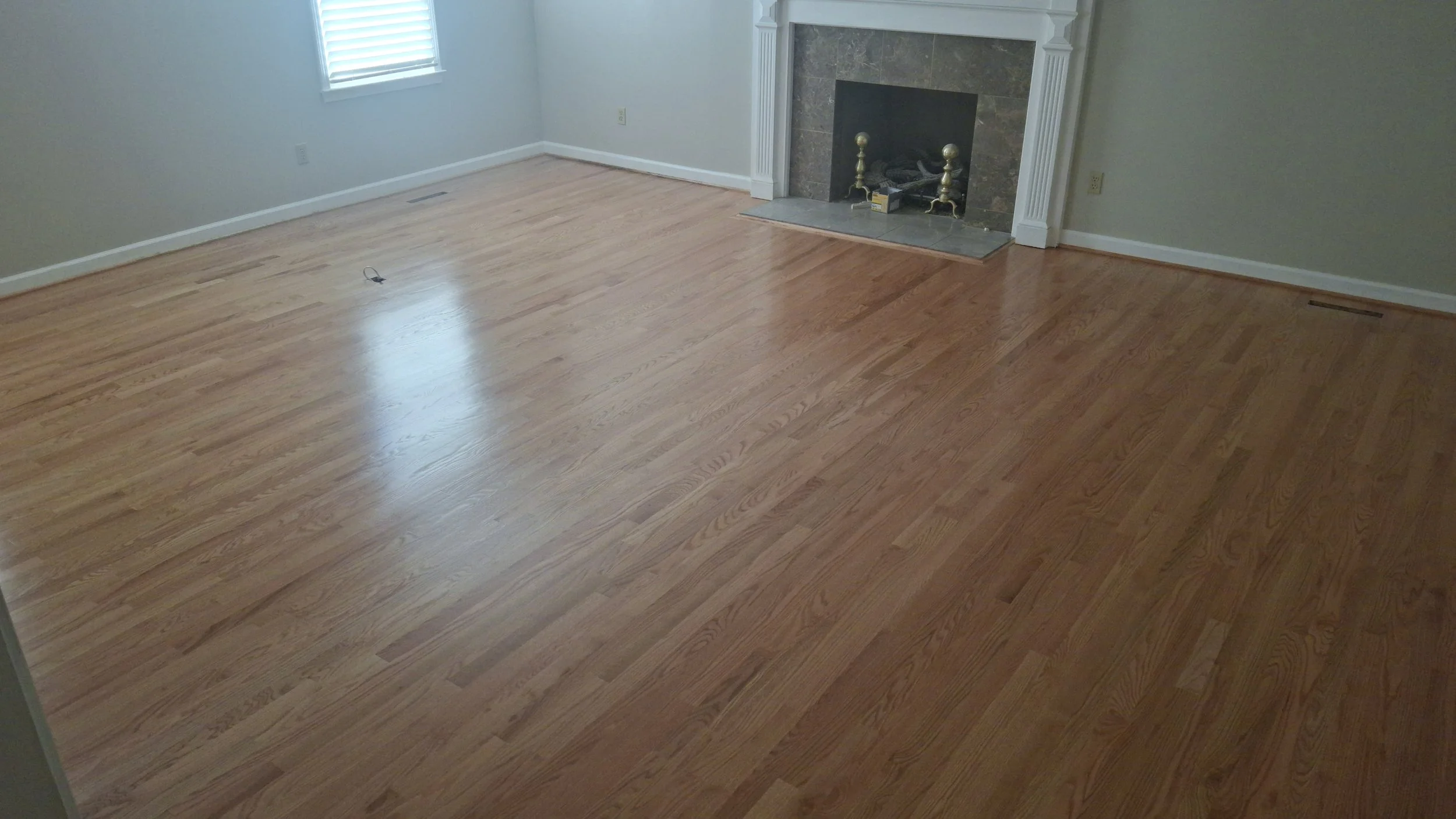 Empty living room with hardwood floors, a fireplace, and a window with blinds.