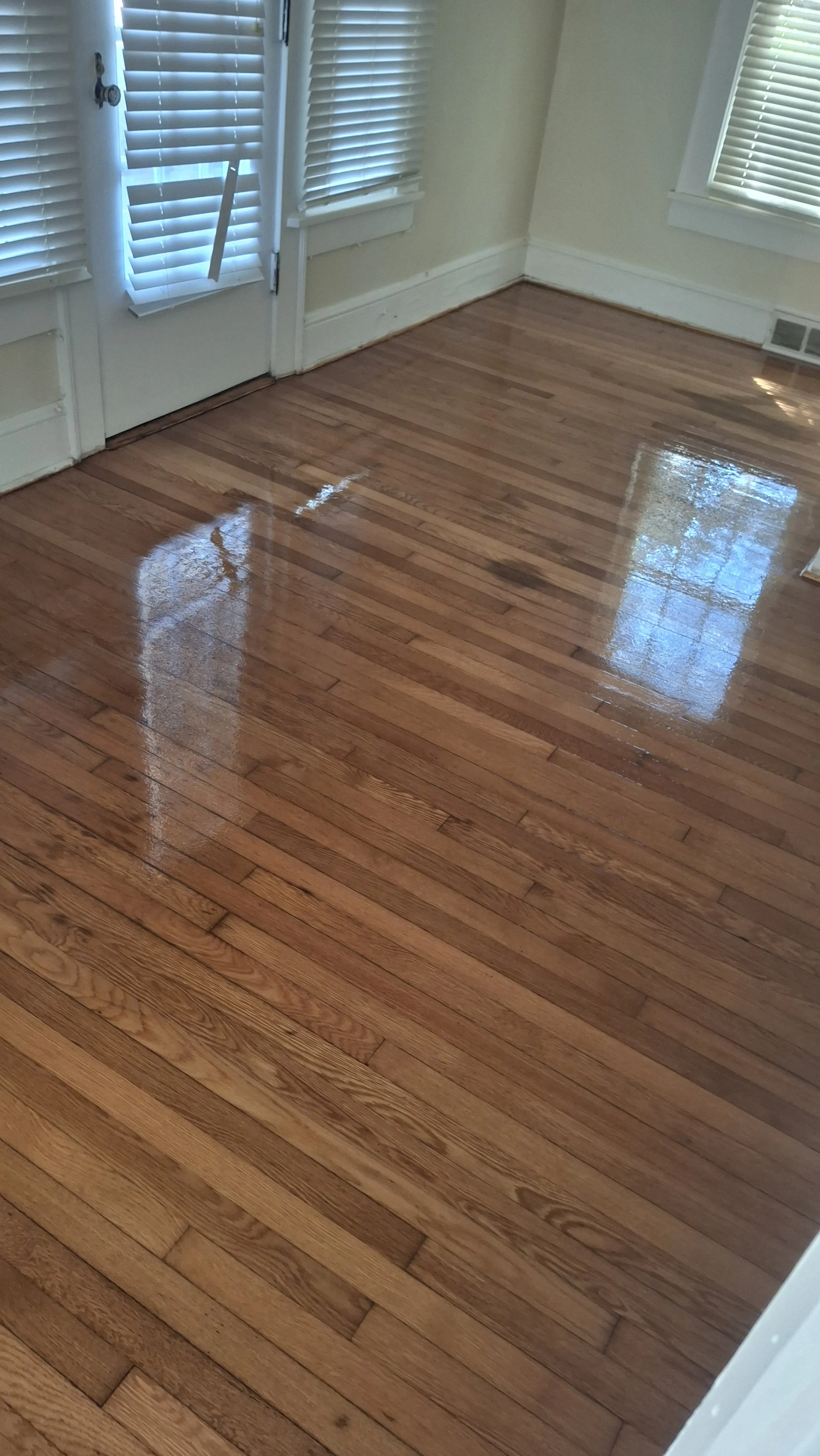 Shiny hardwood floor in a room with a door and windows with blinds.