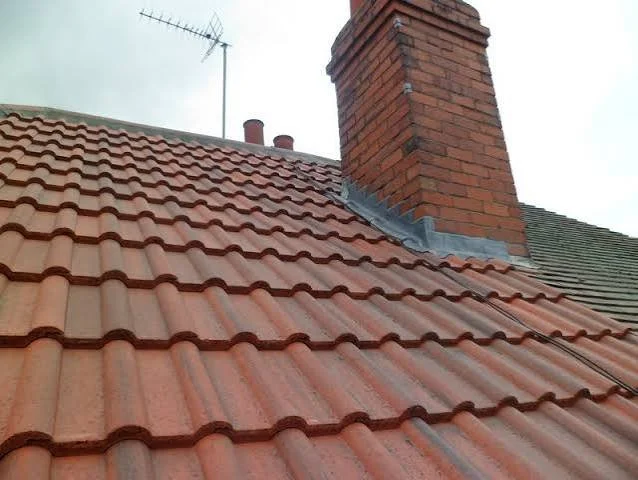 Close-up of a red-tiled roof with a brick chimney and an antenna in the background.