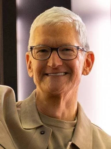 Tim Cook, the openly gay CEO of Apple, smiling indoors in a casual beige jacket.