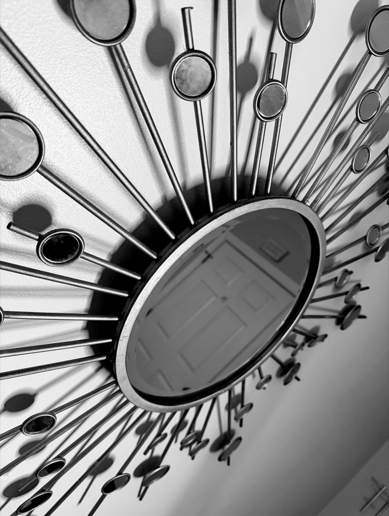 A circular wall mirror surrounded by numerous long, thin metal rods with round mirrors at their ends, arranged in a radiating pattern. Photo by Taneka M. Bennett for the therapy practice Sxuations.com
