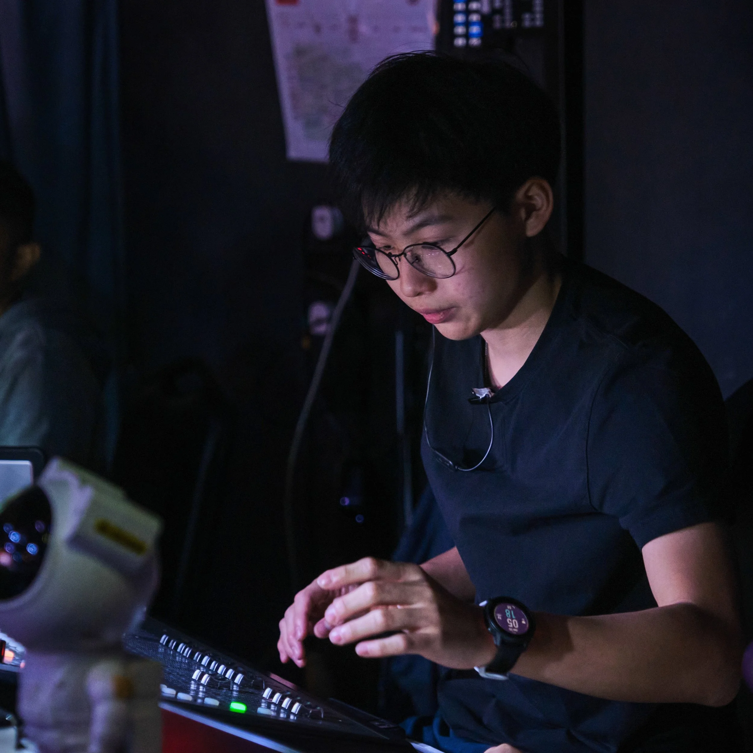 Person wearing glasses working on a computer in a dark room with some lighting, possibly gaming or working late.