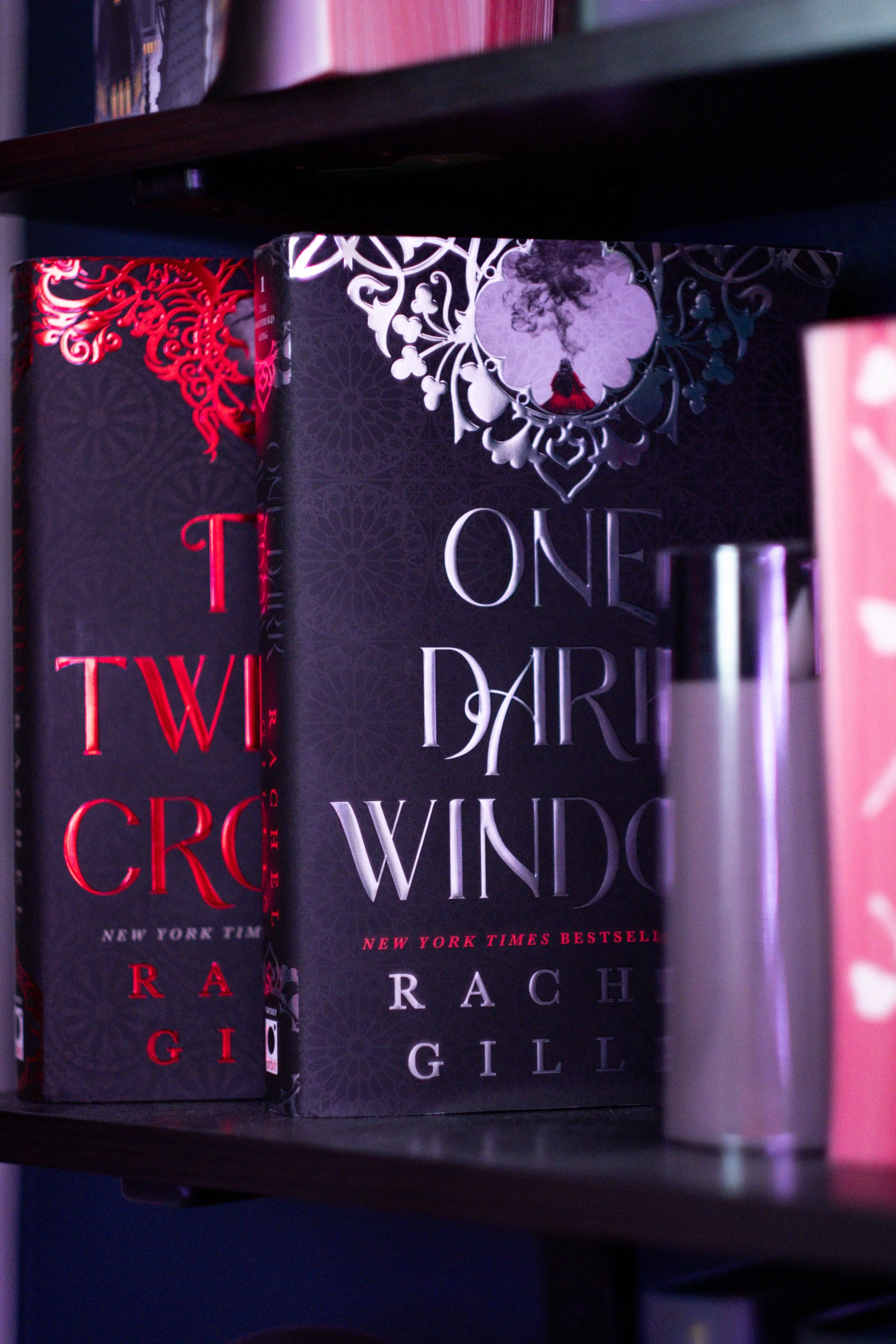 Close-up of several books on a shelf, with the focus on one titled 'One Dark Thrill' by Rachel Gillig, which has a black cover with a purple flower and smoke design.