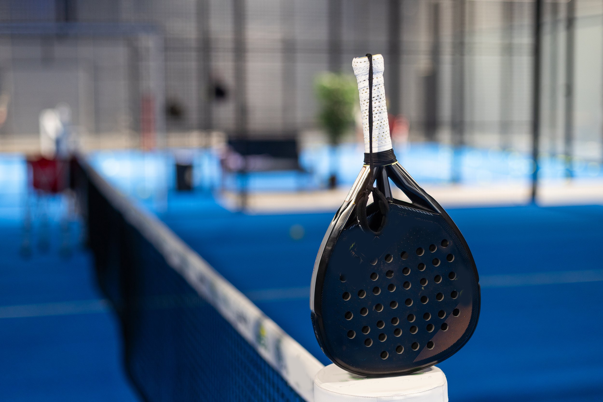 Padel-Schläger in einem Padel-Klub, im Hintergrund ein Netz und blaue Sportmatten.