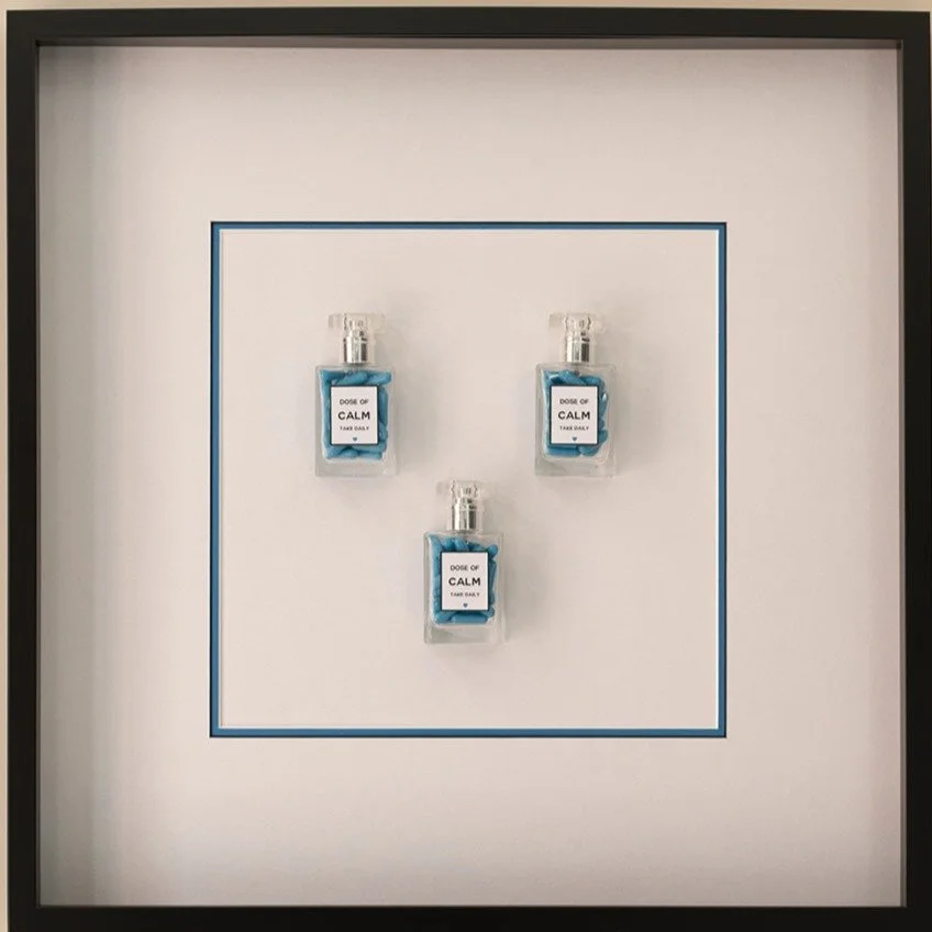 Three small bottles labeled "Dose of Calm" containing blue pills, mounted on a white background with a blue border.